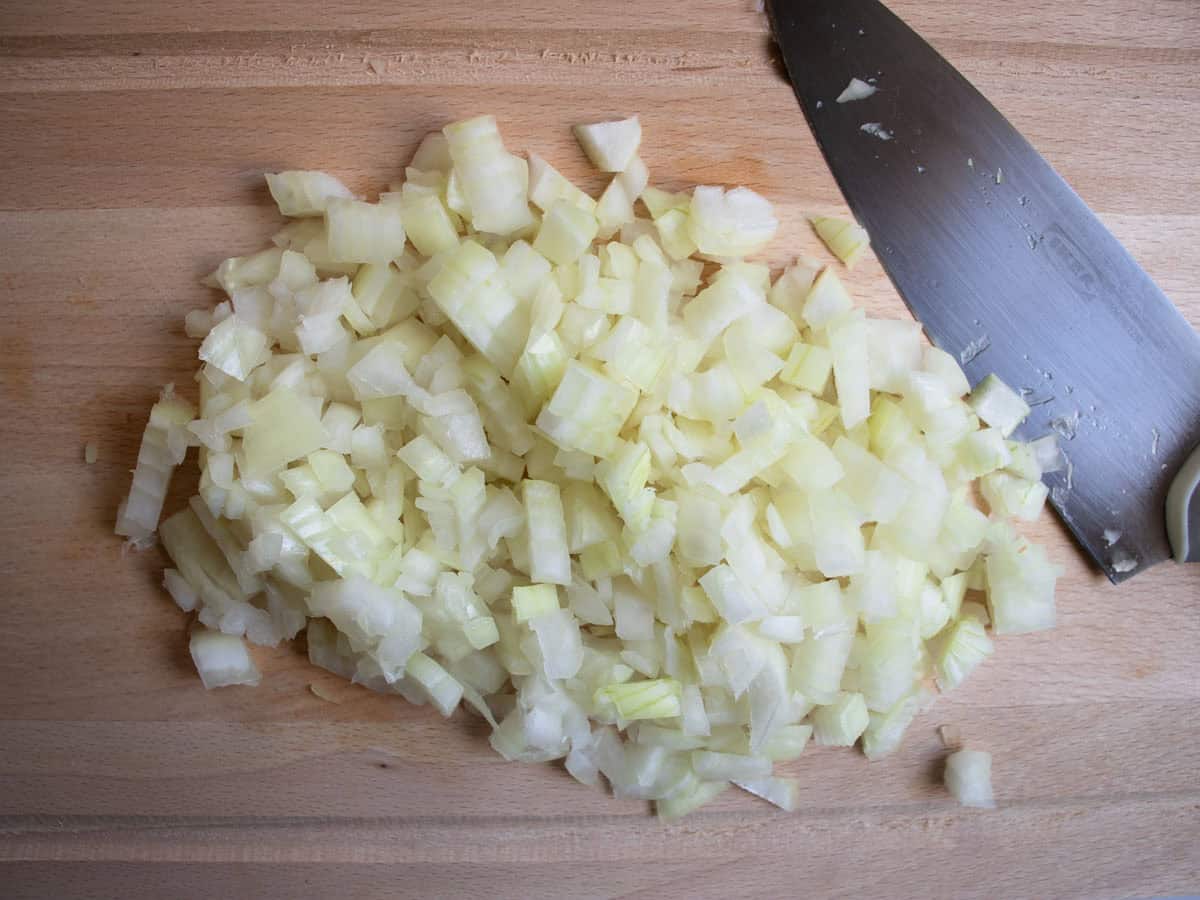 Finely chopped onion on wooden chopping board with chef's knife.
