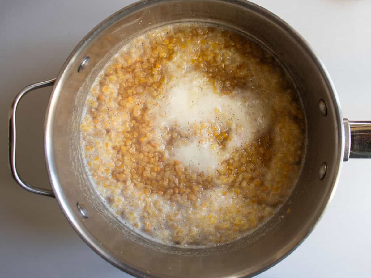 Red lentils simmering in water in stainless steel saucepan.