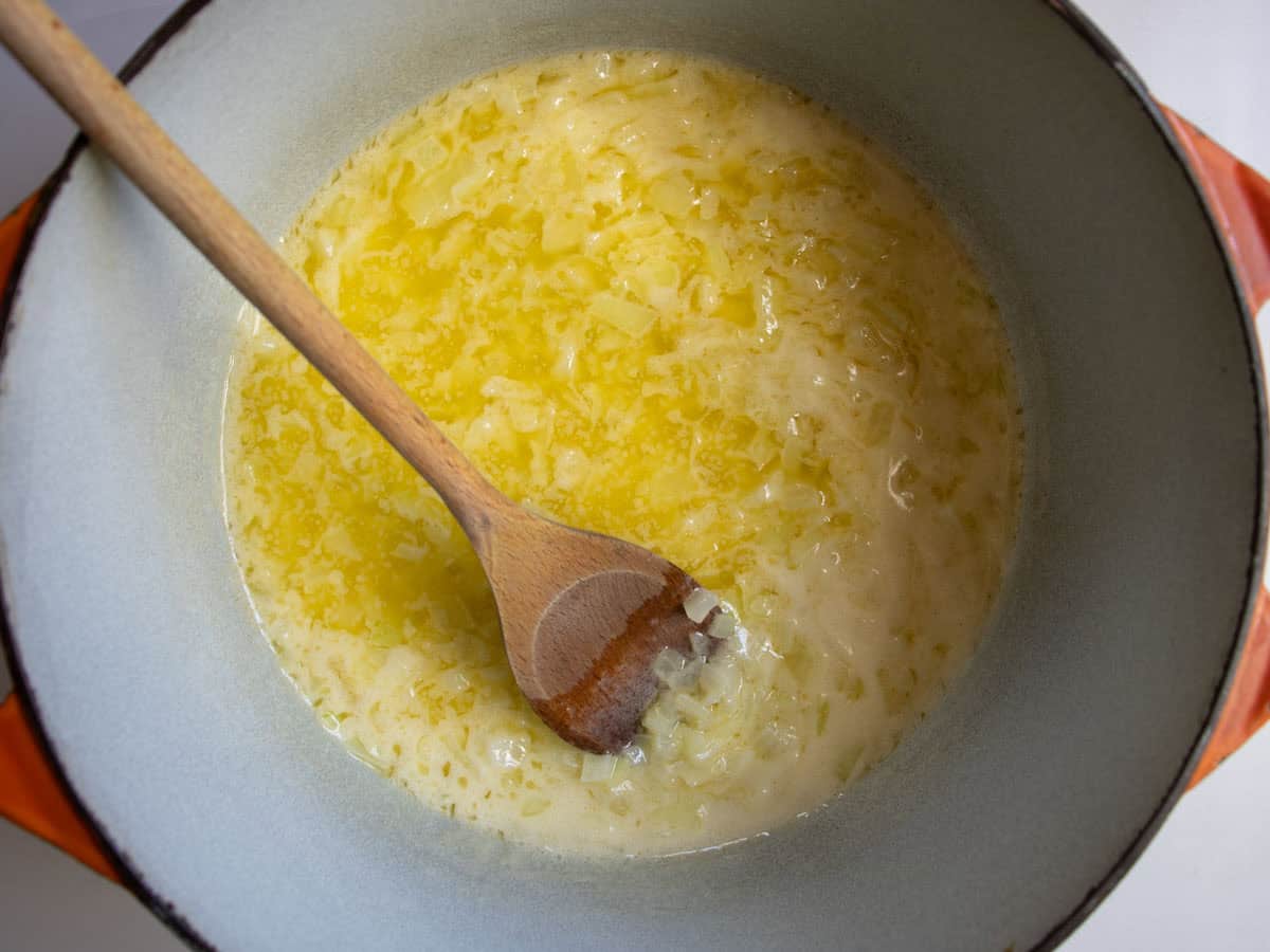 Chopped onion being fried in butter and stirred with wooden spoon.