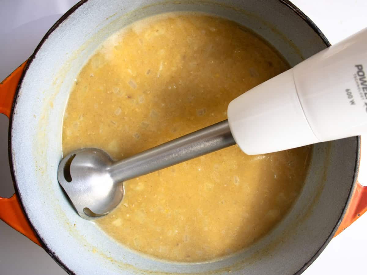 Hand held blender in Lebanese red lentil soup which is in enamelled saucepan.