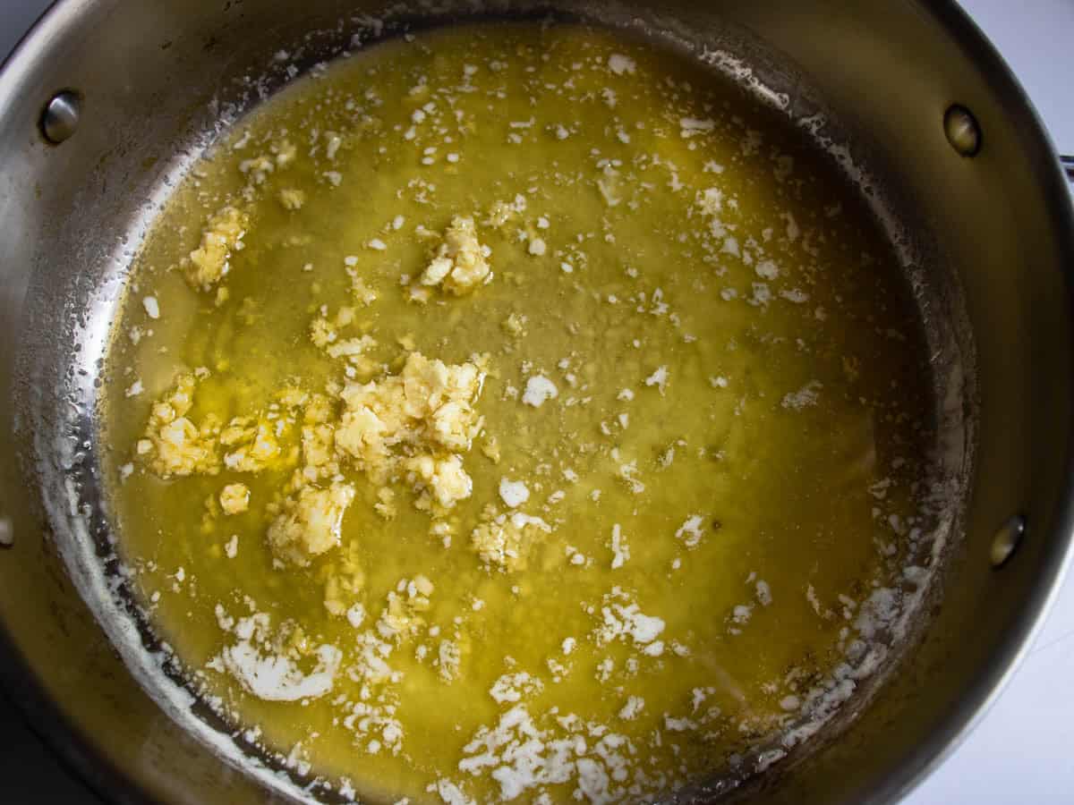 Crushed garlic being heated in melted butter in stainless steel saucepan.