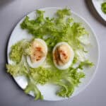 Oeufs mayonnaise sprinkled with paprika and arranged on lettuce on white plate.