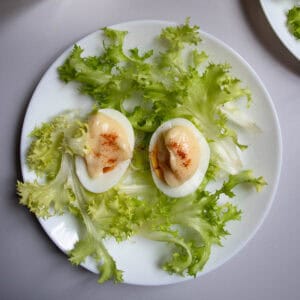Oeufs mayonnaise sprinkled with paprika and arranged on lettuce on white plate.