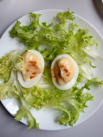 Oeufs mayonnaise sprinkled with paprika and arranged on lettuce on white plate.