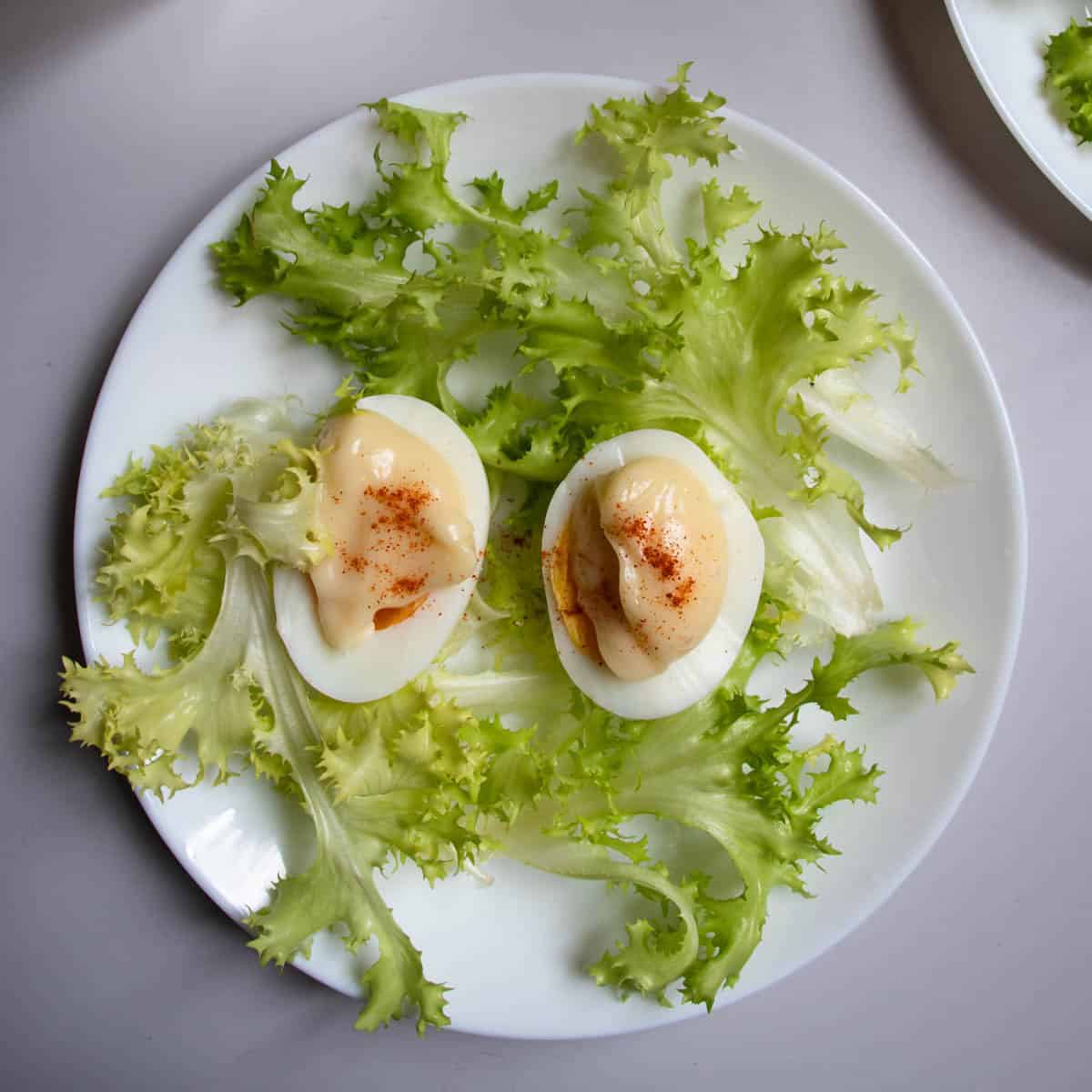 Oeufs mayonnaise sprinkled with paprika and arranged on lettuce on white plate.