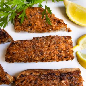 Mashed sardines on sourdough toast cut into fingers, next to slices of lemons and sprig of parsley.