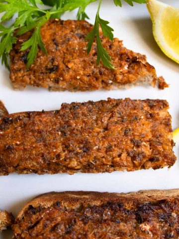 Mashed sardines on sourdough toast cut into fingers, next to slices of lemons and sprig of parsley.