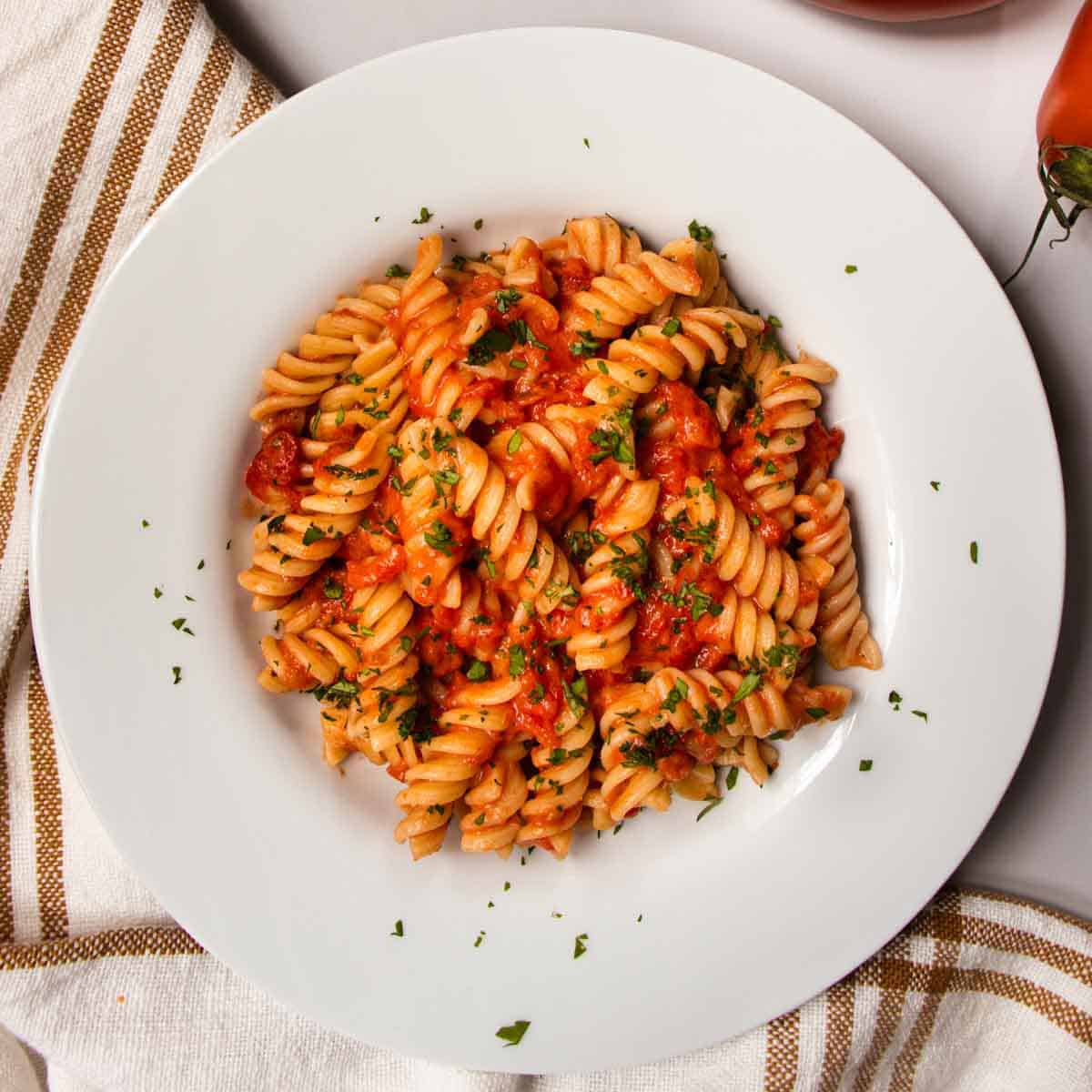 Creme Fraiche Tomato Pasta in white dish, next to fresh tomatoes.