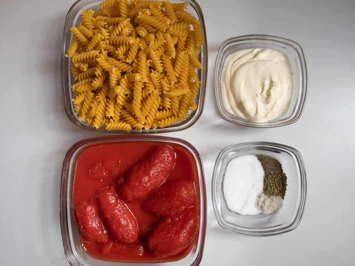 Fusilli pasta, tinned tomatoes, creme fraiche, salt, pepper, sugar and dried oregano all in square glass dishes.