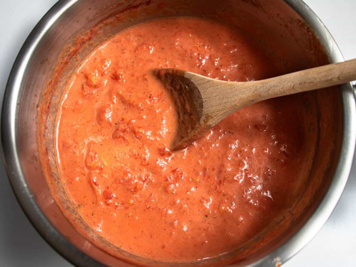 Creme Fraiche Tomato Pasta sauce in stainless steel saucepan being stirred with wooden spoon.
