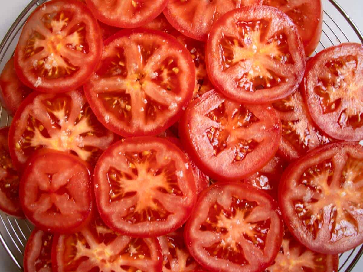 Tomatoes sliced in rounds and sprinkled with salt laid flat on round wire tray.