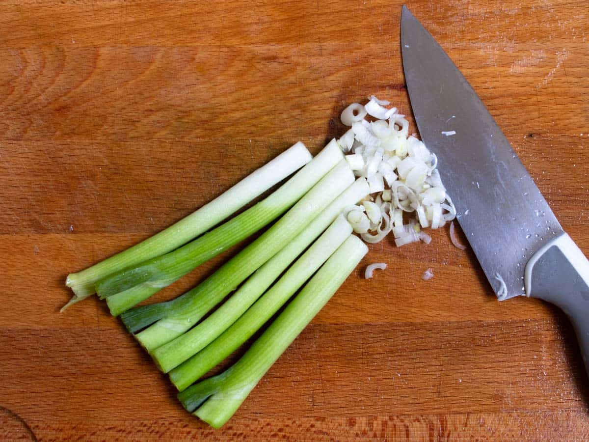 Green onions being finely chopped with chef's knife.