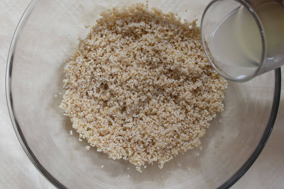 Lemon juice being poured from a glass onto bulgur wheat in glass mixing bowl.