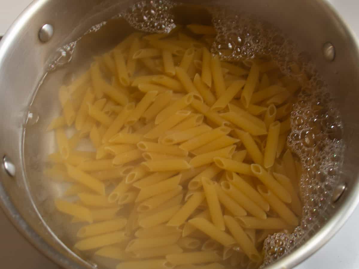 Penne pasta in hot water in stainless steel saucepan.