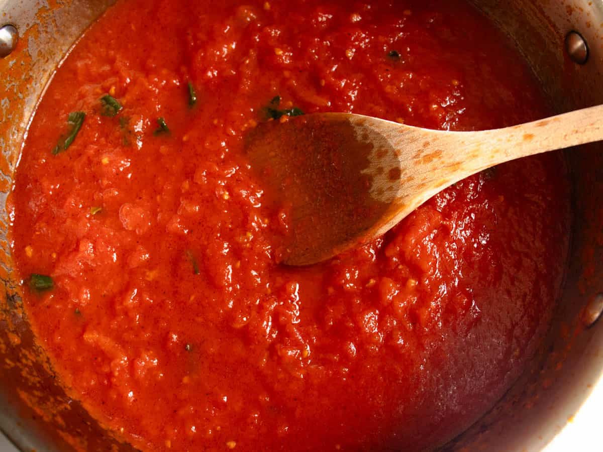 Penne Napoli sauce in stainless steel saucepan being stirred with wooden spoon.