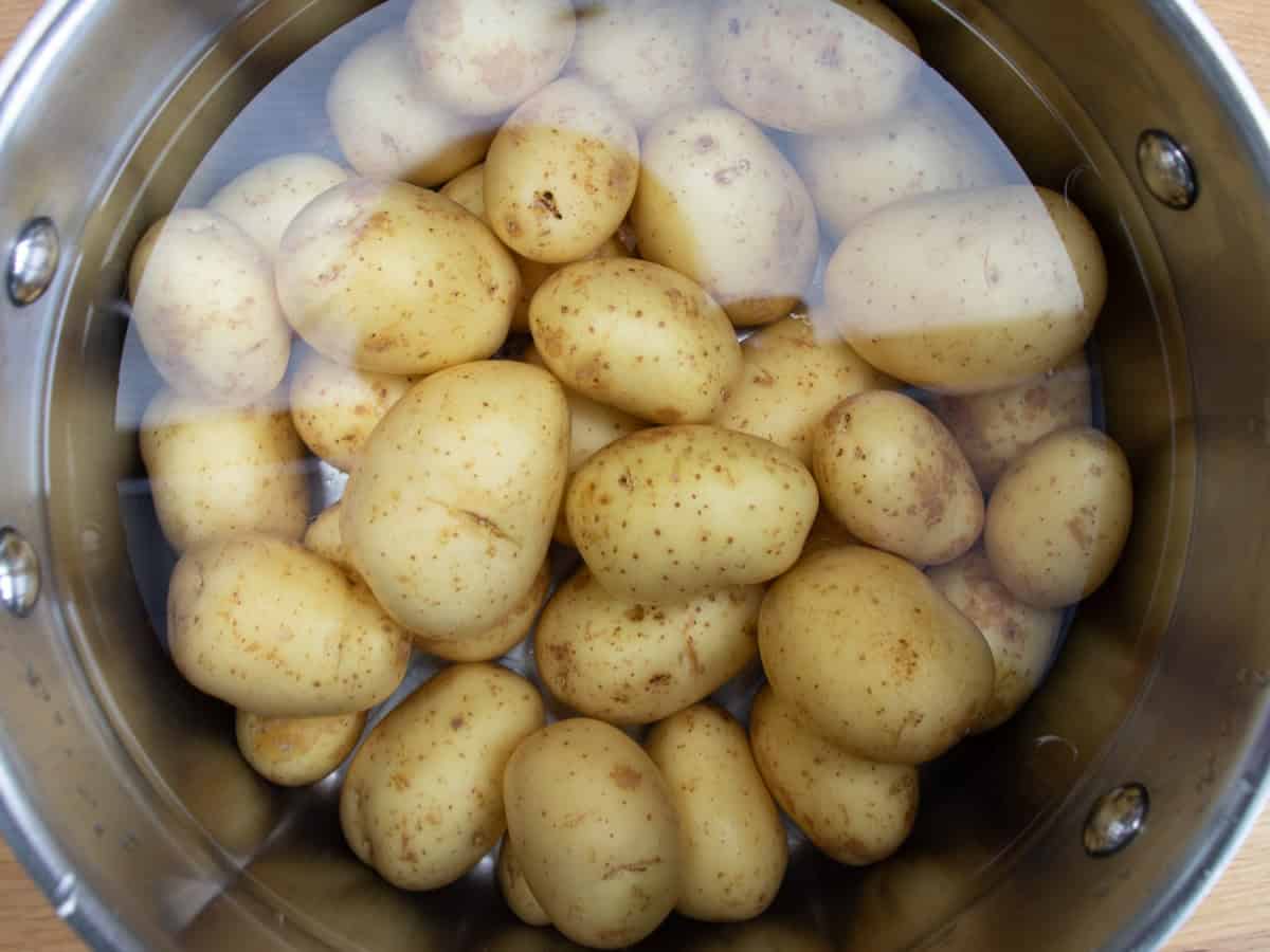 New potatoes in cold water in stainless steel saucepan.