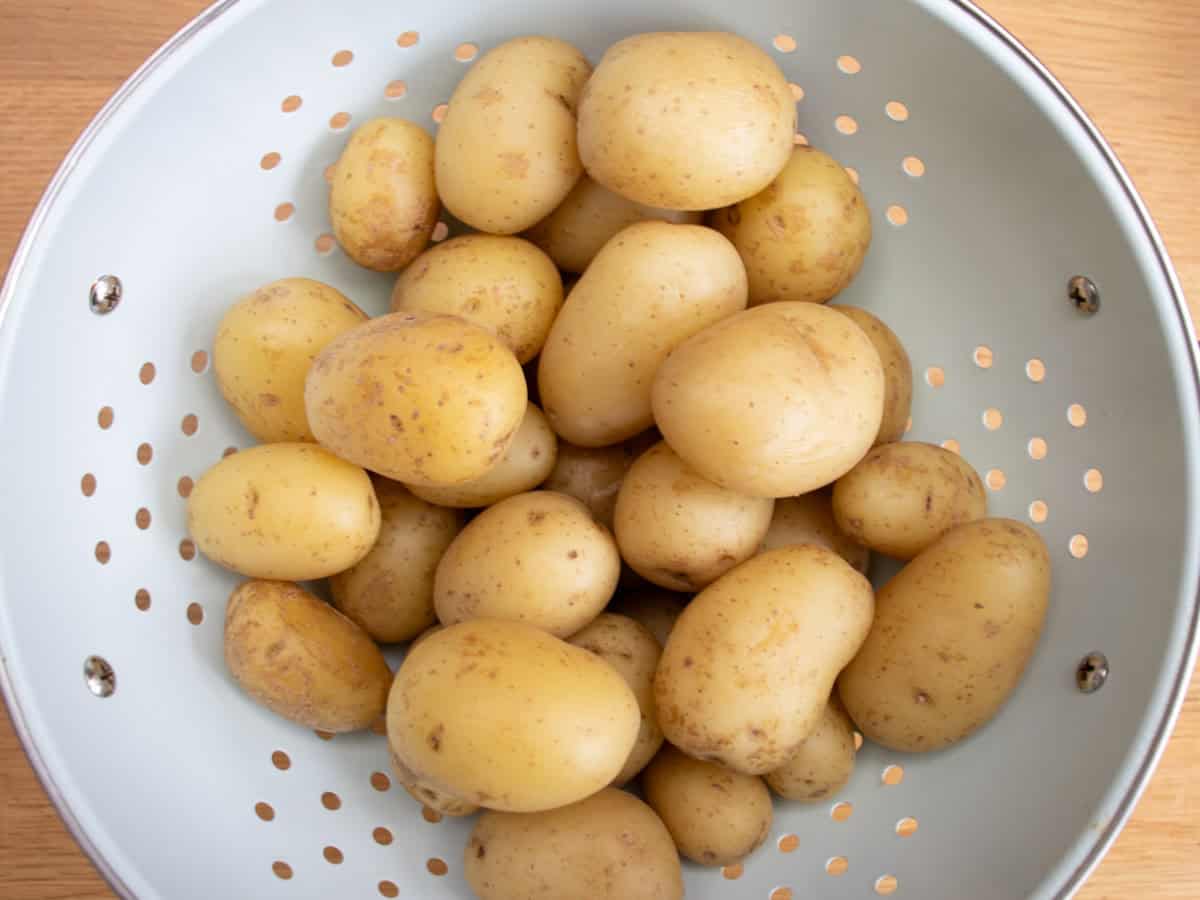 Cooked new potatoes in blue enamelled colander.