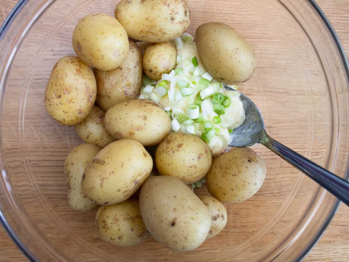 Cooked new potatoes, chopped spring onions and mayonnaise about to be stirred with spoon in mixing bowl.