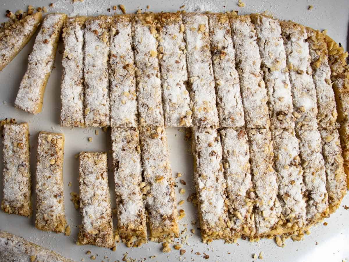 Walnut shortbread cookie dough covered in chopped walnuts and sugar sliced into baton shapes.