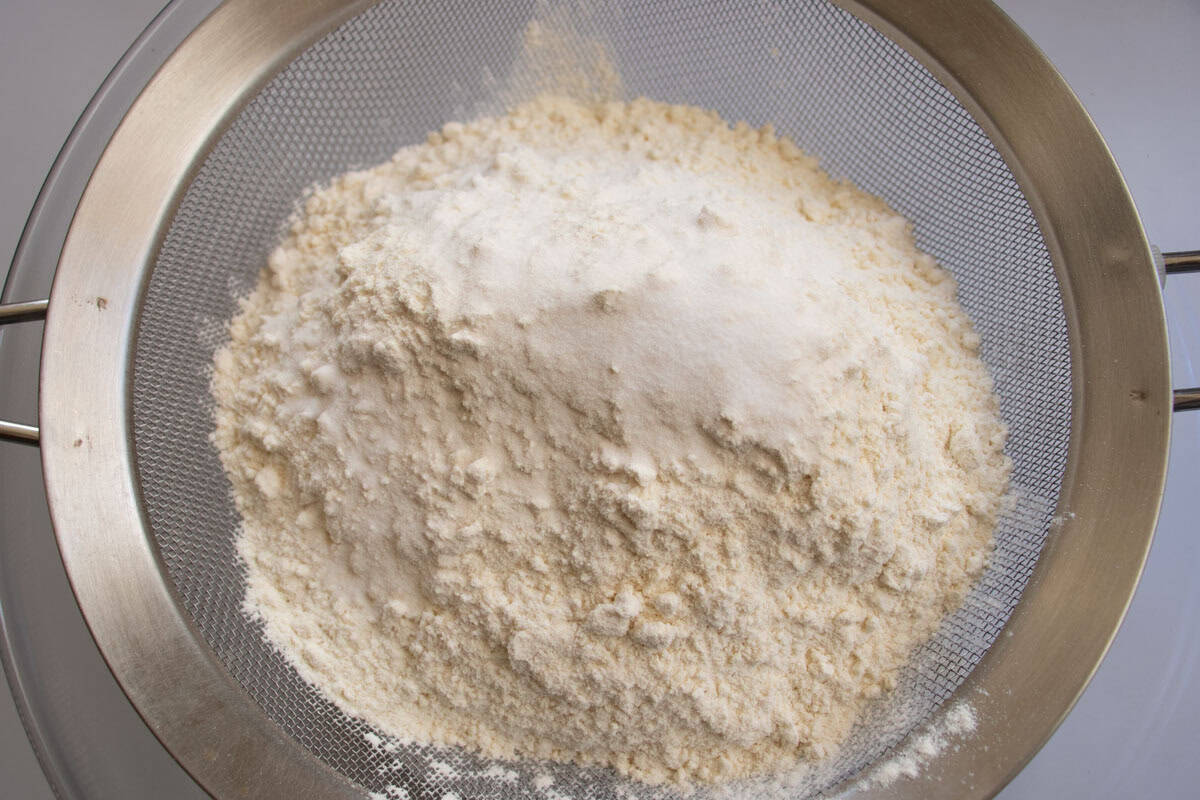 Flour and bicarbonate of soda in sieve held above glass mixing bowl.