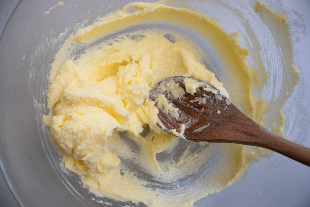 Butter and sugar being stirred with wooden spoon in glass mixing bowl.