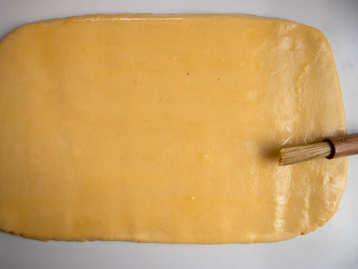 Rolled out cookie pastry being brushed with beaten egg.
