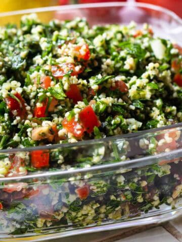 Lebanese tabbouleh in a square glass dish on tiled surface.