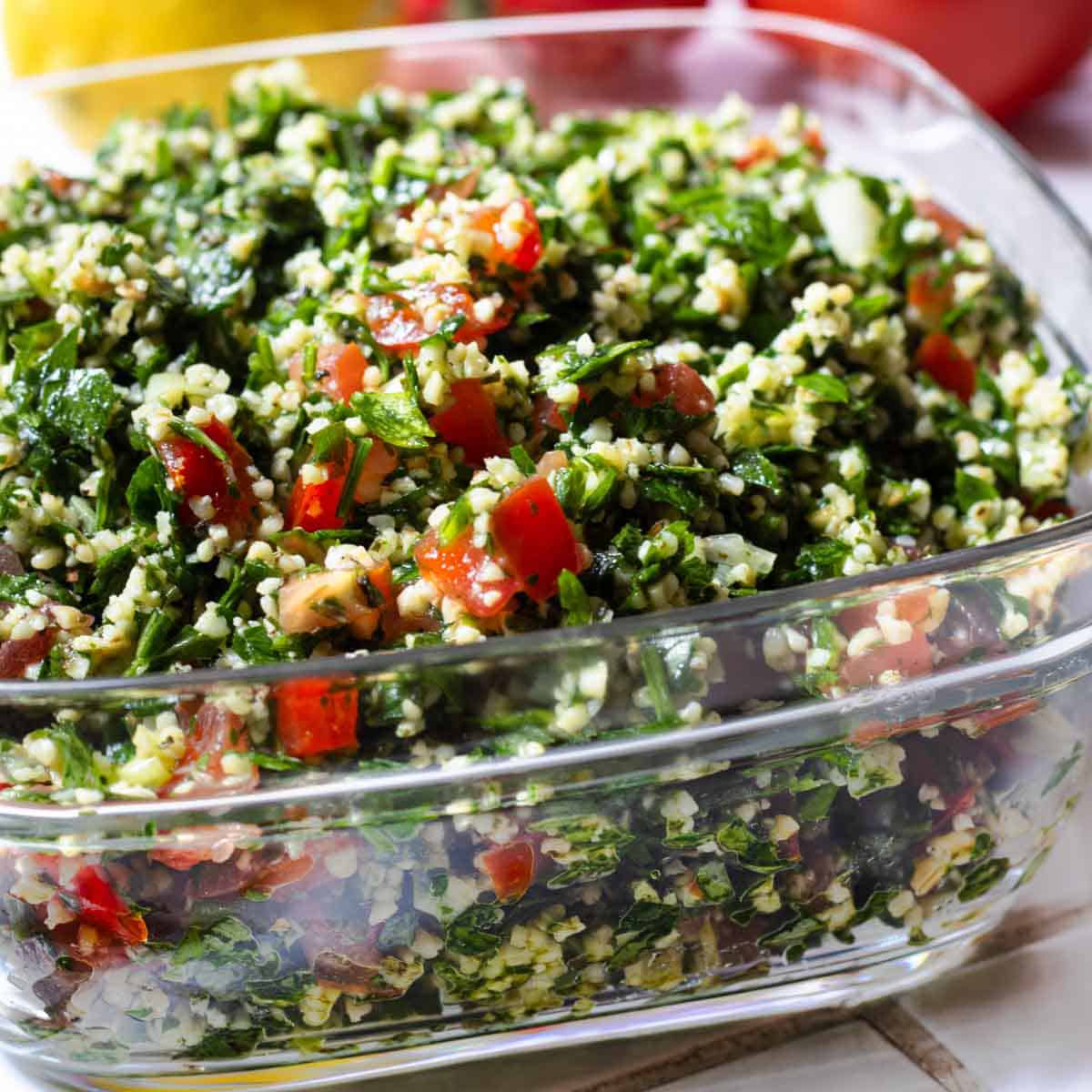 Lebanese tabbouleh in a square glass dish on tiled surface.