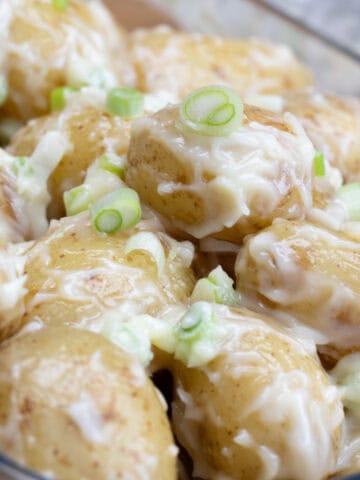 Potato salad with mayonnaise and spring onions in glass dish.