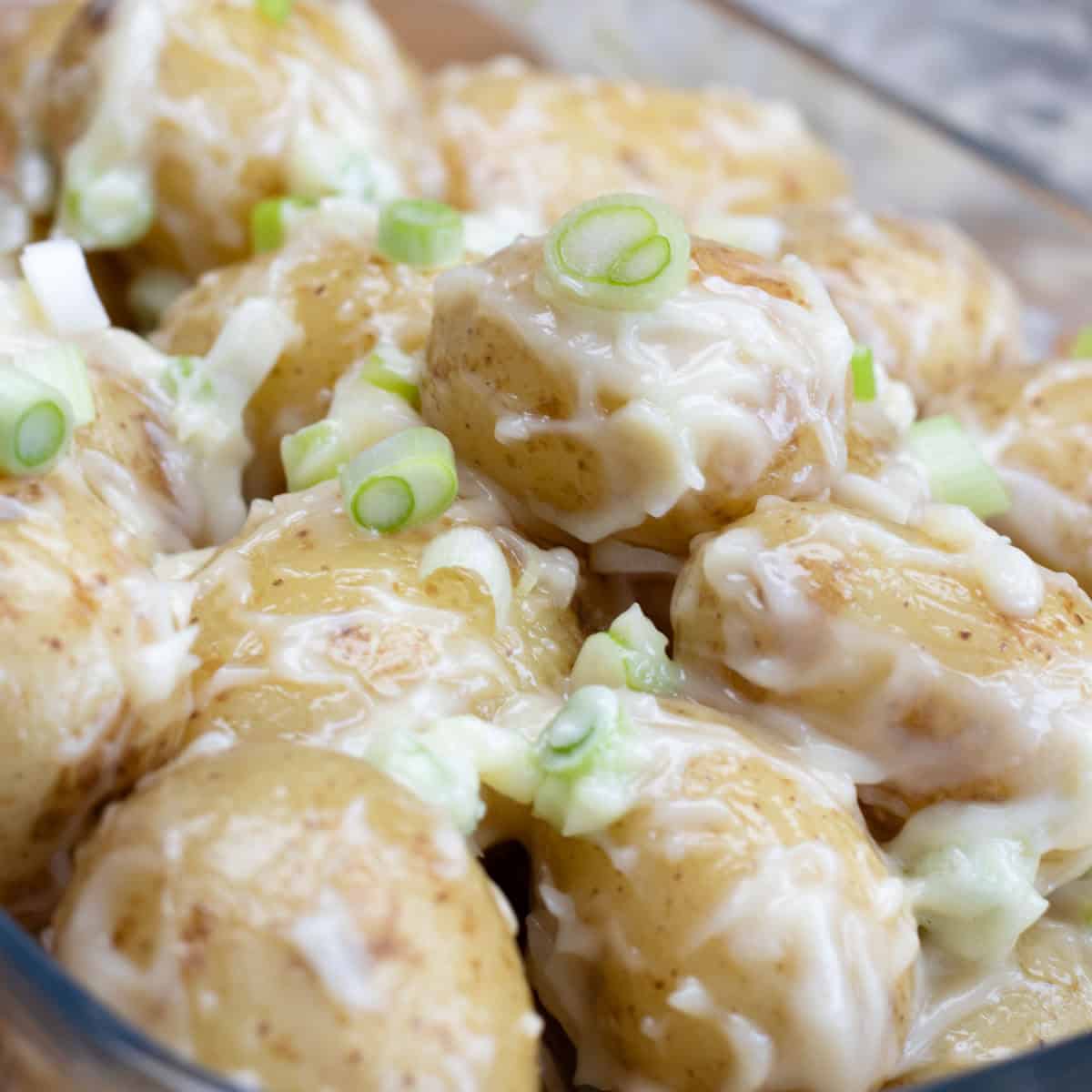 Potato salad with mayonnaise and spring onions in glass dish.