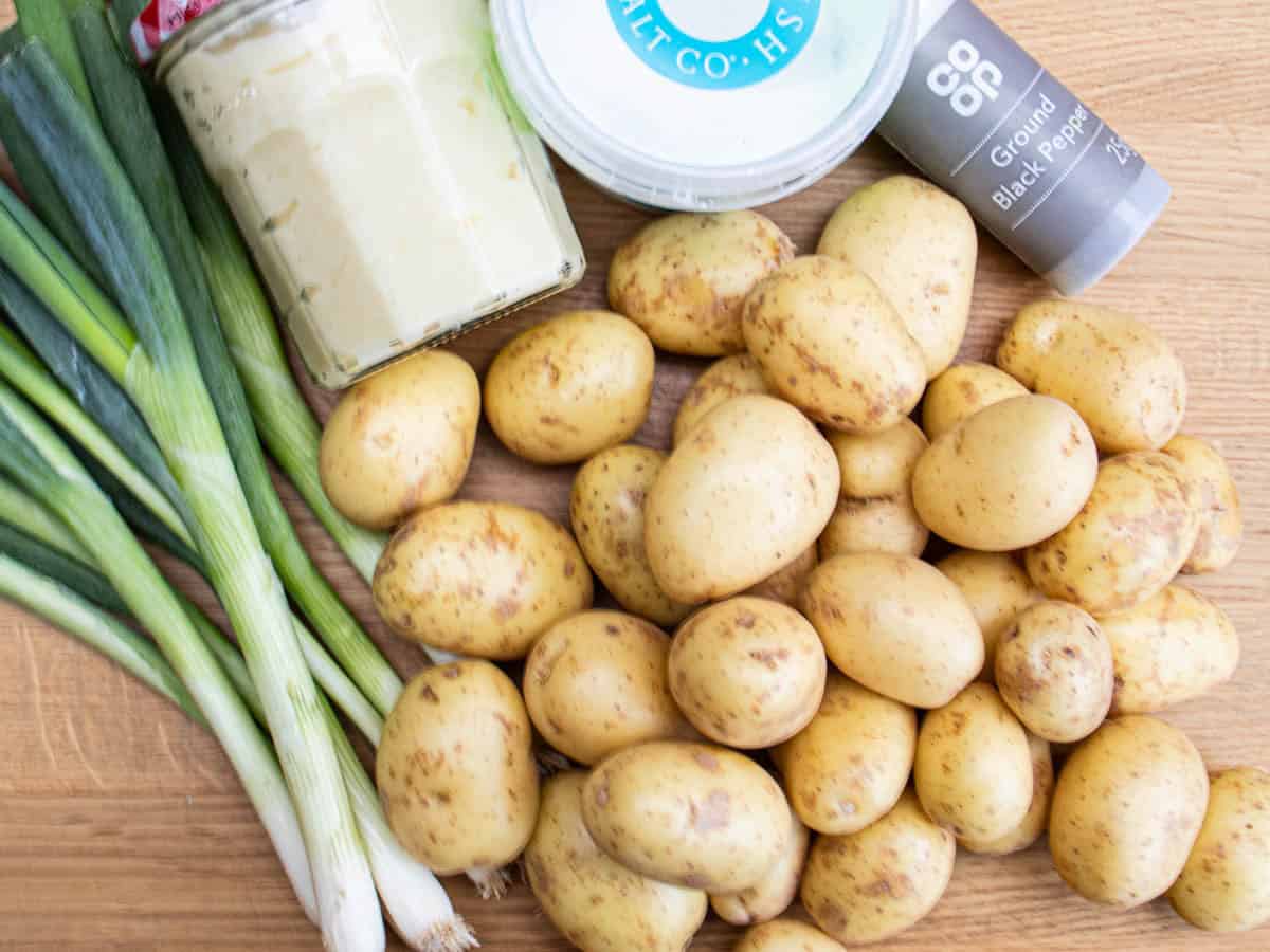 Spring onions, new potatoes, jar of mayonnaise, tub of salt and black pepper laid out on wooden surface.