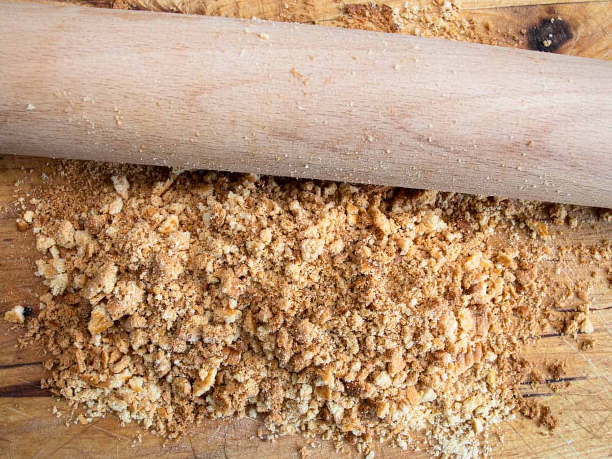 Rolling pin crushing biscuits on a wooden board.
