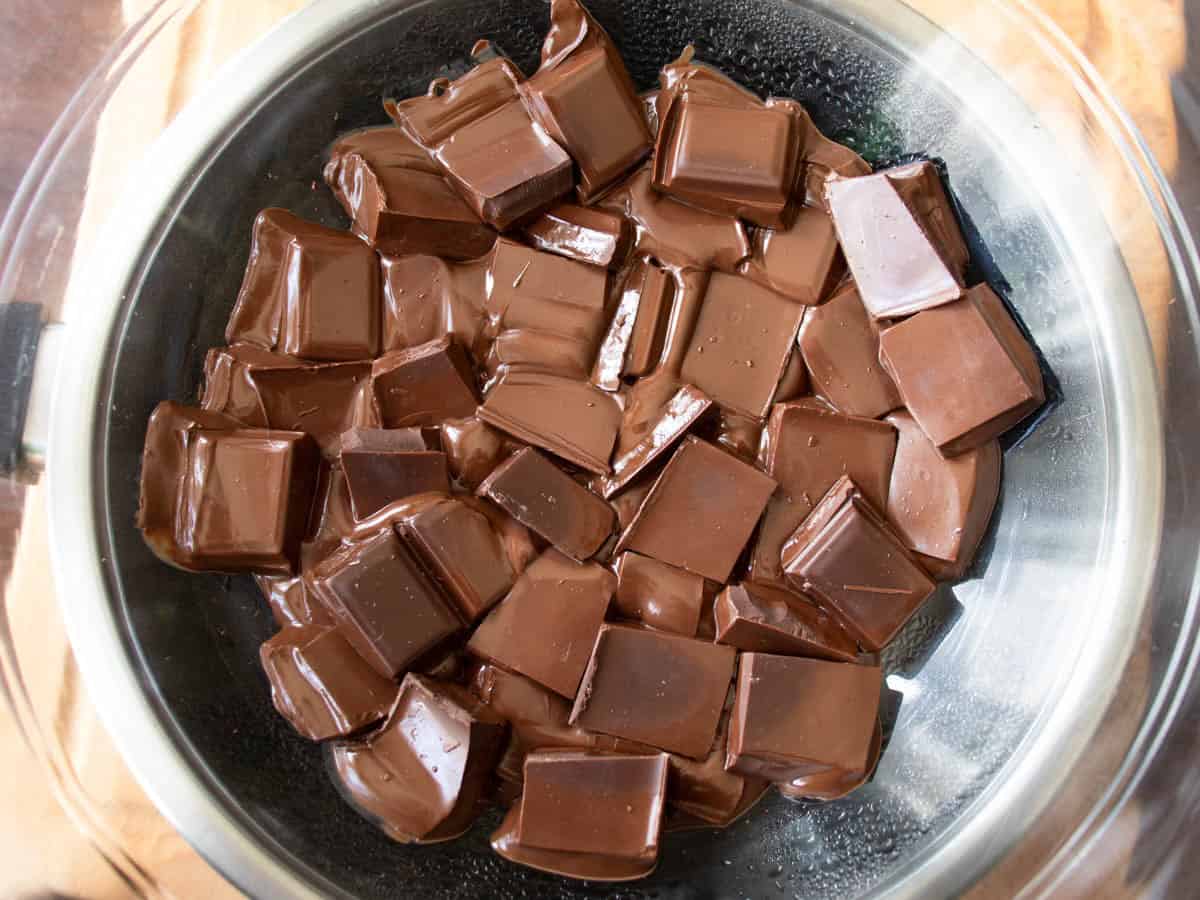 Broken pieces of chocolate melting in glass bowl over saucepan.