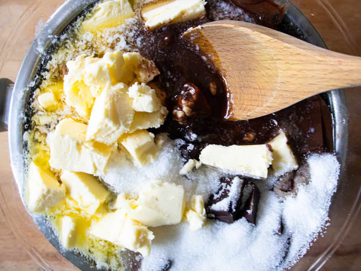 Egg being stirred by wooden spoon into chocolate mixture in glass mixing bowl.