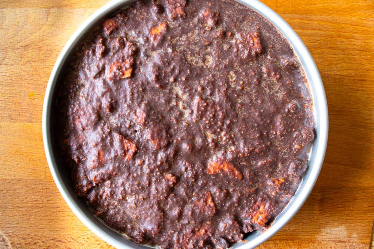 Chilled round baking tin filled with chocolate biscuit cake mixture on wooden surface.