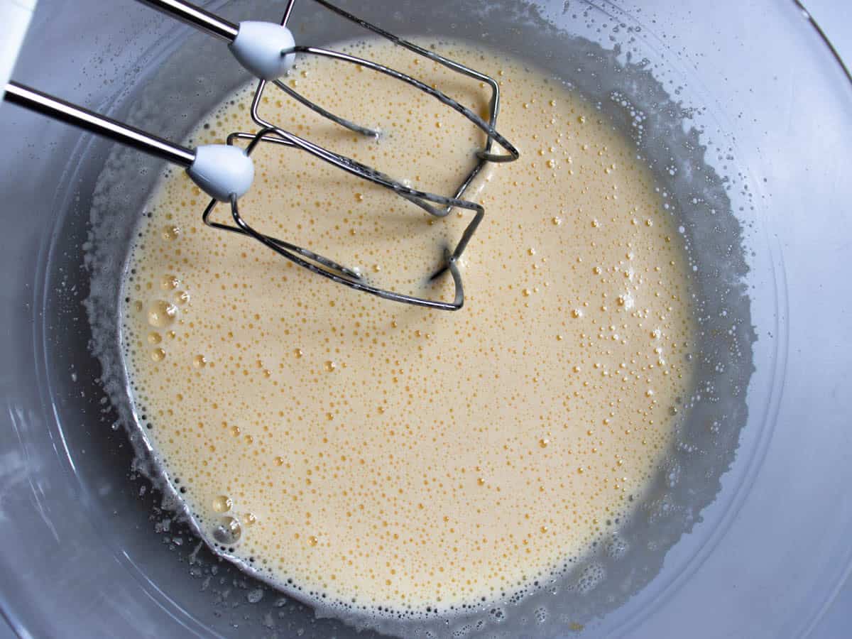 Electric whisk attachments in whisked egg and sugar mixture in glass mixing bowl.