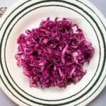 Red cabbage coleslaw on green striped plate with caraway seeds to side of plate.