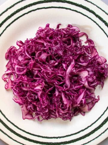 Red cabbage coleslaw on green striped plate with caraway seeds to side of plate.