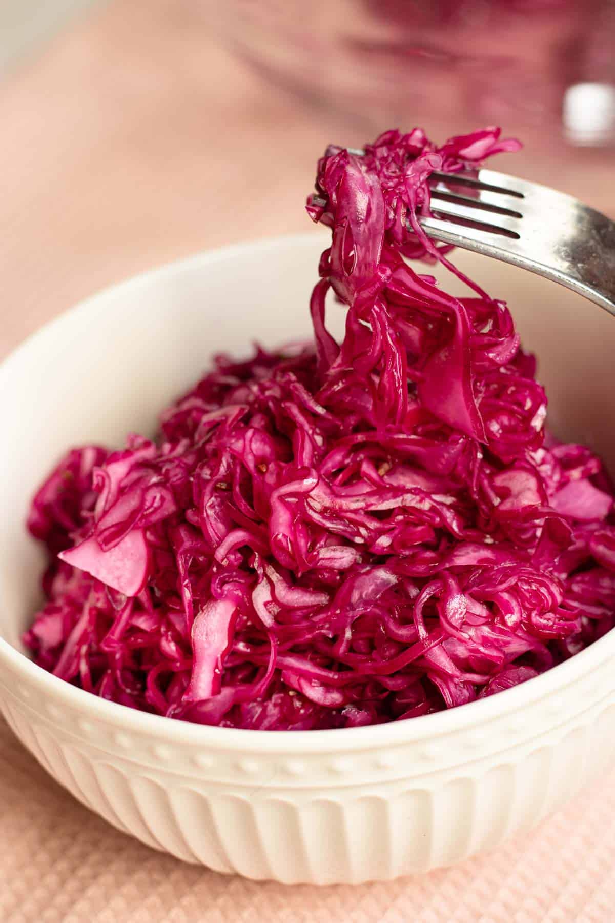 Red cabbage coleslaw being lifted by fork from a small white bowl.