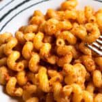 Spirali pasta coated in red pesto sauce, a fork lifting one piece of pasta, on striped dish.