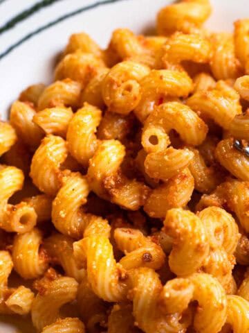 Spirali pasta coated in red pesto sauce, a fork lifting one piece of pasta, on striped dish.